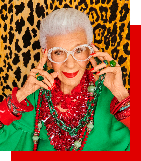 Image of Iris Apfel wearing iris x Zenni dressed to the nines oval glasses #4453123, wearing a brightly-colored outfit against a leopard print background.