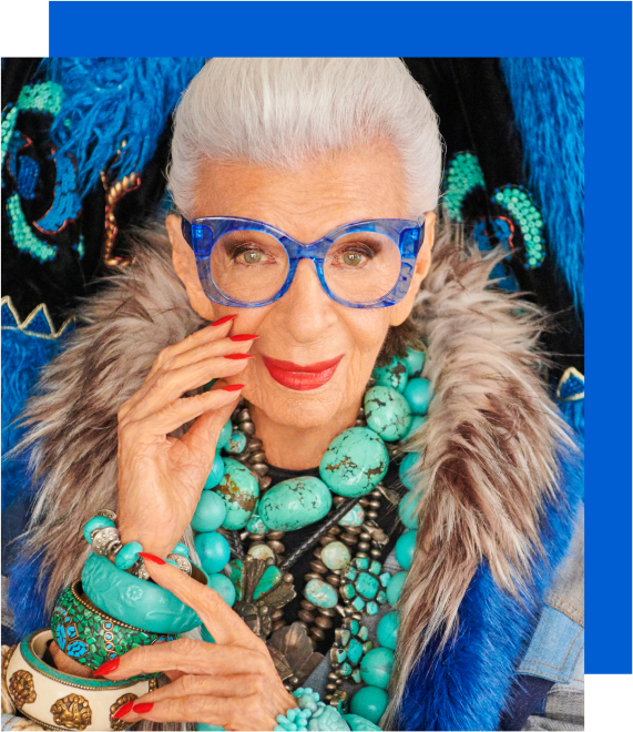 Image of Iris Apfel wearing Zenni What’s New Pussycat cat-eye glasses #4452616. She is wearing large turquoise jewelry and is standing in front of a tie dye-printed wall.
