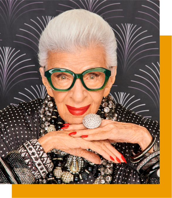 Image of Iris Apfel wearing Zenni smashing! cat-eye glasses #4452824. She is wearing a large diamond ring, her hair is slicked back and she’s in front of a black wallpapered background. 