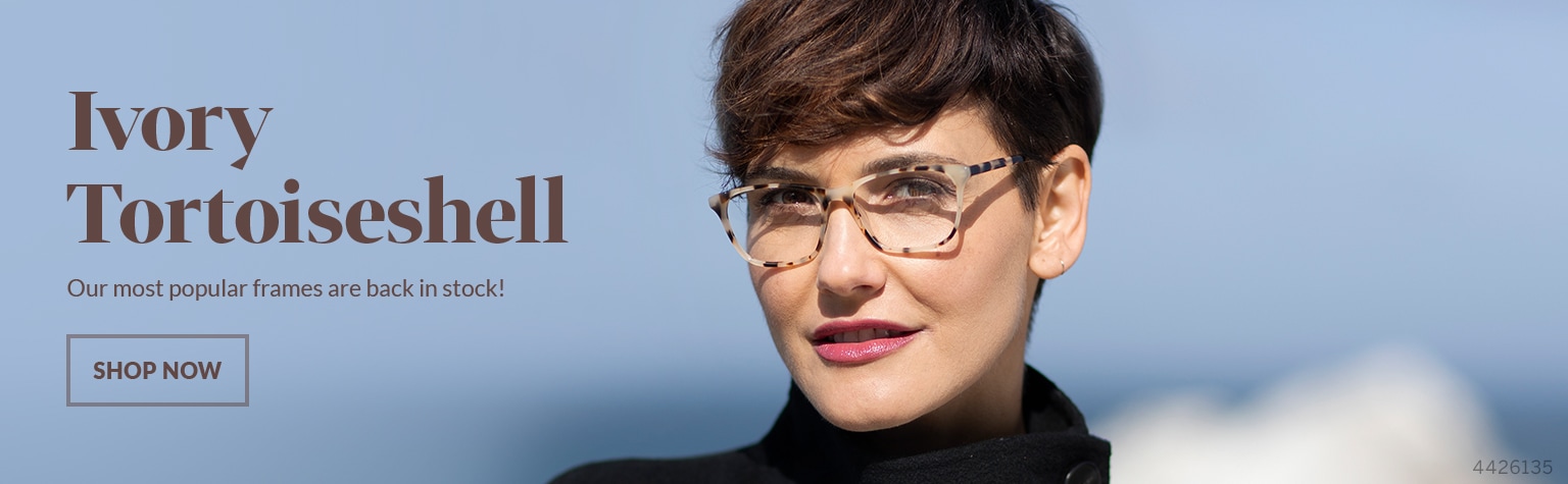 Woman with short brown hair wears a black top with ivory tortoiseshell square glasses #4426135 stands with a rugged beach in the background.