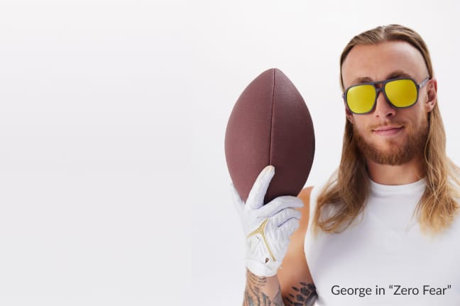 George Kittle, holding an American football, wearing Zenni aviator sunglasses ‘Zero Fear’ with gold mirror tinted lenses.