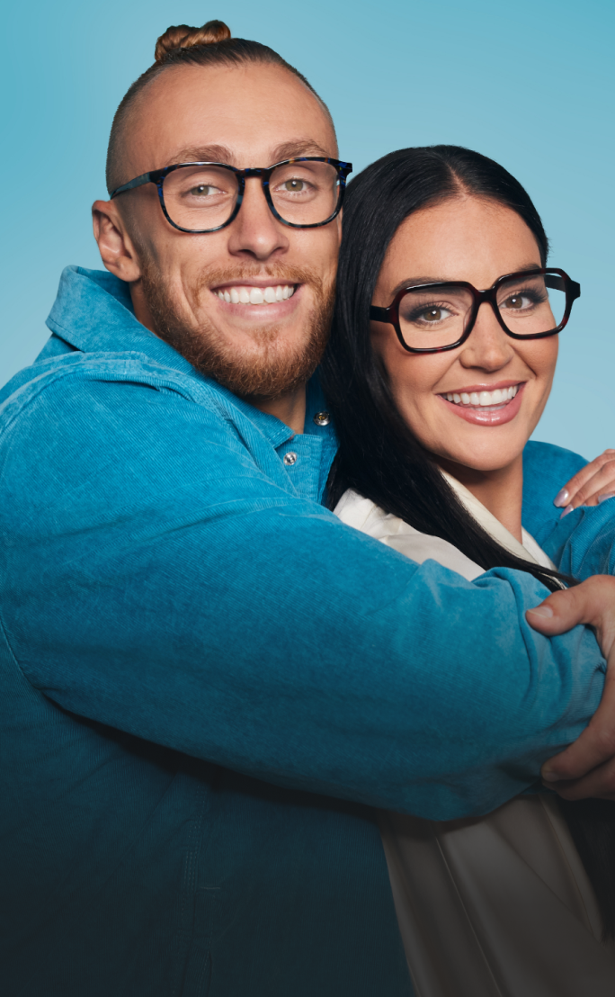 George Kittle and wife Claire, wearing Zenni glasses, smiling and embracing against a light blue background.