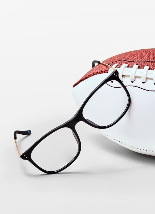 Close-up of a pair of black-frame Kittles Collection Zenni glasses, resting against a white and red football on a white background.(The People's Frames & #7826125)