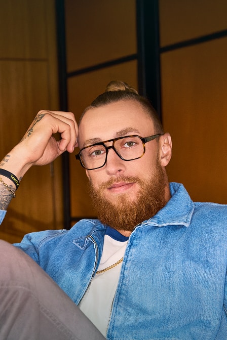 George Kittle sitting indoors wearing tortoiseshell aviator-style Zenni glasses and denim collared shirt.