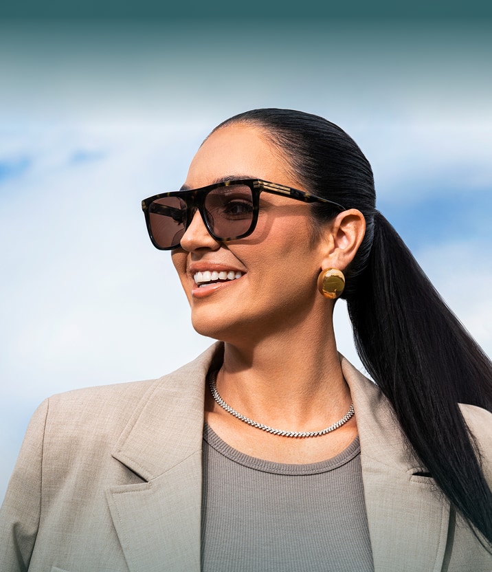 Claire Kittle smiling in oversized Zenni sunglasses and a neutral blazer against a sky background.