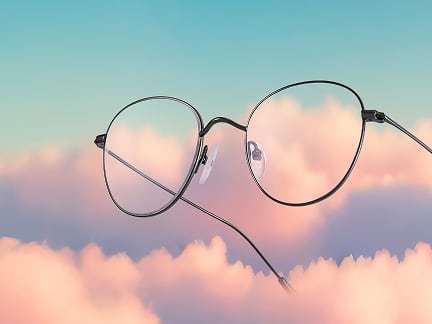 Round titanium glasses float on a background of pink clouds and blue sky.