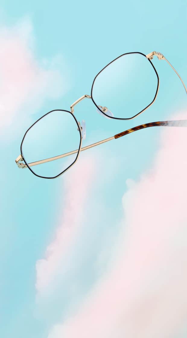 Black and gold metal geometric glasses with tortoiseshell temples. Background of blue sky with fluffy clouds.