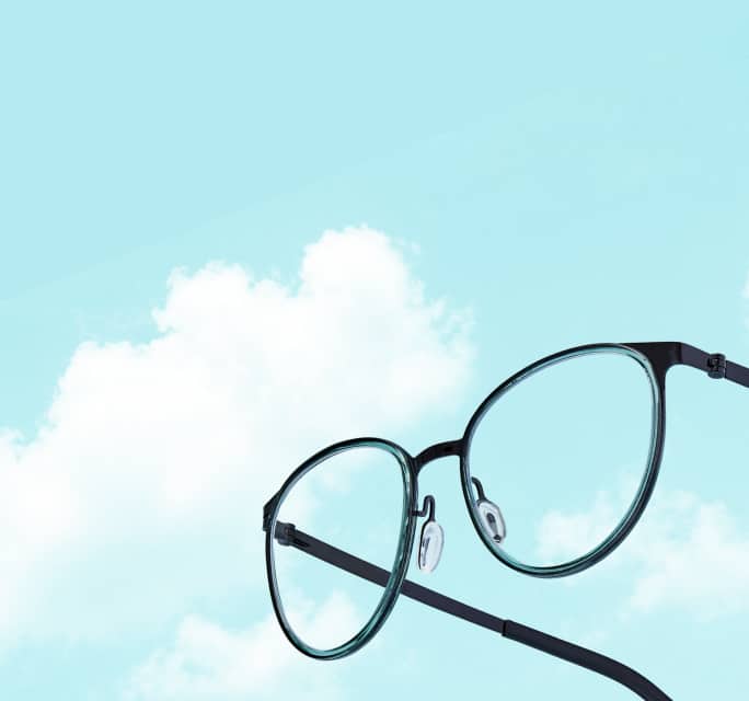 Close-up of rose gold cat-eye eyeglasses with thin metal rims and translucent pink temples, floating on a solid light blue background.