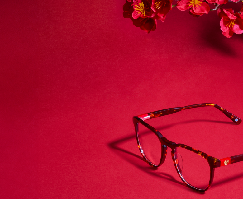 Tortoiseshell glasses with a dragon inlay on the temple, on a red background with flowers in the corner.