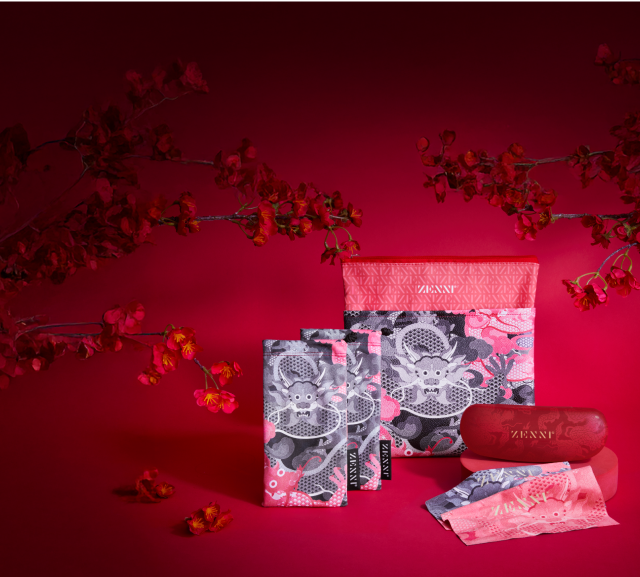 A matching accessory set includes a Zenni-branded glasses pouch, cloth, and case. The items have intricate dragon-themed designs in gray, pink, and red hues. Cherry blossom branches frame the scene.