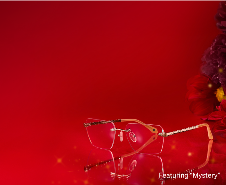 Rimless eyeglasses with a golden frame on a red background with decorative arms and floral accents.