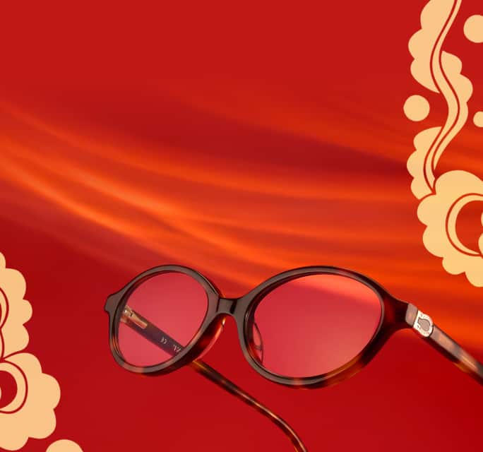 Oval tortoiseshell Zenni glasses with a gold horseshoe detail on the temple arm, surrounded by a gold floral horse motif over a red background.