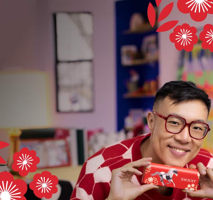 Artist Zipeng Zhu wearing red square frame Zenni glasses, holds a Zenni eyeglasses case he designed featuring a bold horse and floral illustrations.