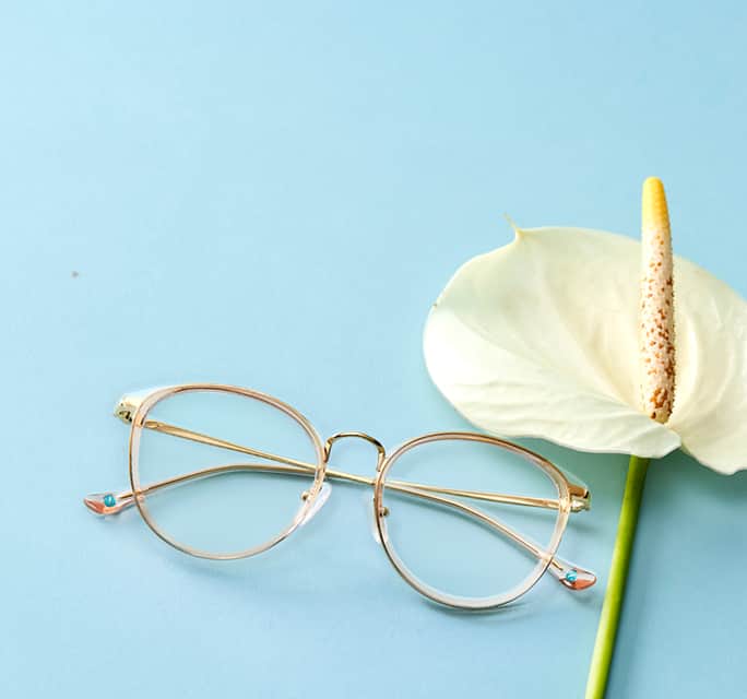 Round transparent and gold Zenni glasses on blue surface with a white lily.