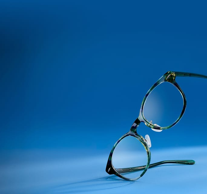 A pair of round, green tortoise-shell glasses standing upright on a blue surface against a matching blue background.