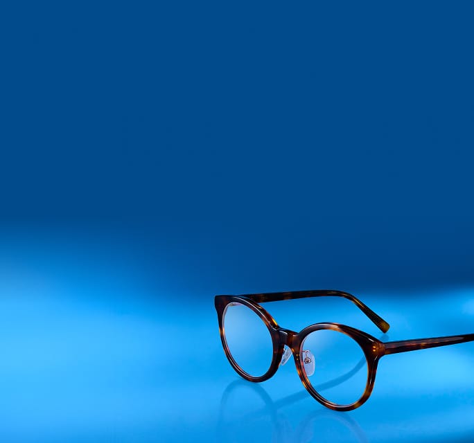 A pair of round, tortoise-shell patterned glasses resting on a reflective blue surface with the numbers '2026' displayed in the top left corner.