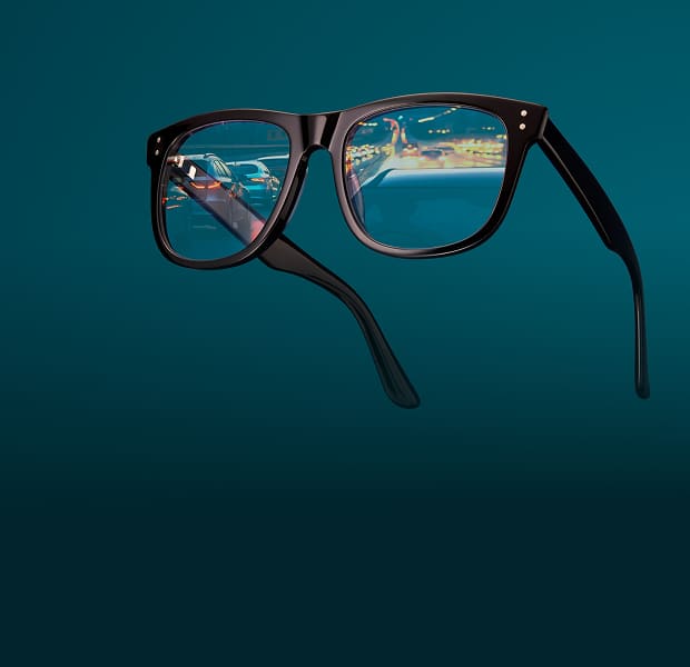 Square black glasses with nearly clear night driving lenses, reflecting a street at night. Background is dark teal.