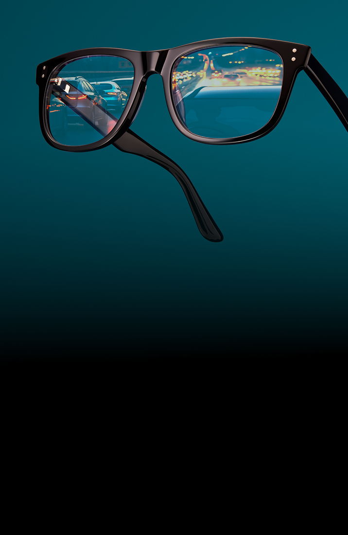 Square black glasses with nearly clear night driving lenses, reflecting a street at night. Background is dark teal.