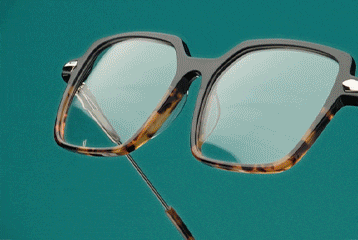 Lunettes carrées oversized avec haut de monture noir, bas en écaille de tortue et branches métalliques fines sur fond vert sarcelle.