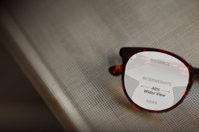 Tortoiseshell glasses with Premium Progressive lenses showing viewing zones =  'DISTANCE, 40% Wider View, INTERMEDIATE, NEAR' against a textured gray backdrop.