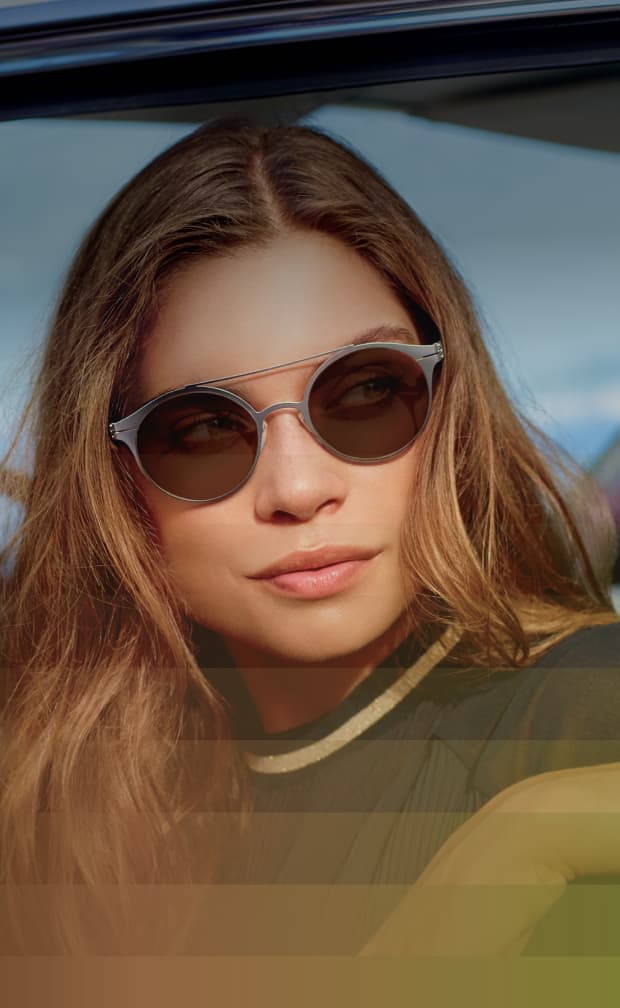 A woman with long brown hair wearing light-adaptive Transitions® sunglasses, which darken in bright sunlight.