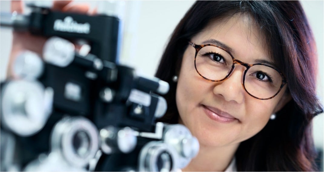  Image of an optical professional standing behind an eye test machine, wearing Zenni glasses..