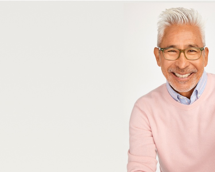 A smiling man with gray hair in a pink sweater wearing green transparent rectangle glasses.