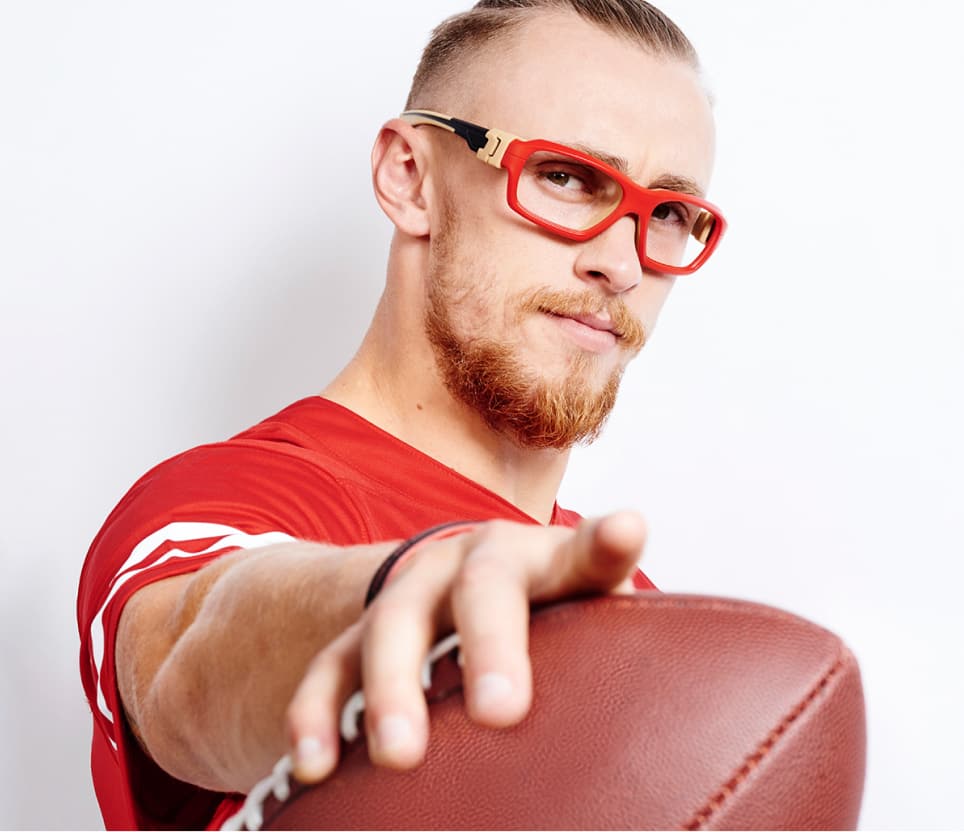 Image of George Kittle wearing Zenni protective sports goggles, holding a football.