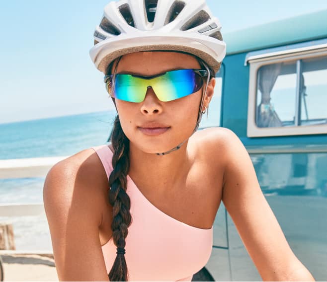 Image of a woman wearing Zenni sports sunglasses while riding a bike near the beach.