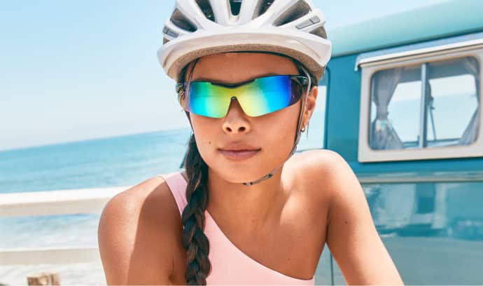 Image of a woman wearing Zenni sports sunglasses while riding a bike near the beach.