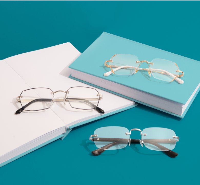 Three pairs of reading glasses resting on a stack of books on a light blue background.