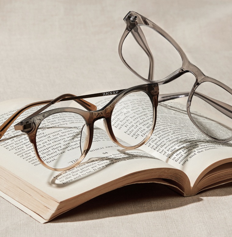 Image of two pairs of Zenni glasses, round glasses #7823412 and rectangle glasses #125012, stacked on top of an open book.