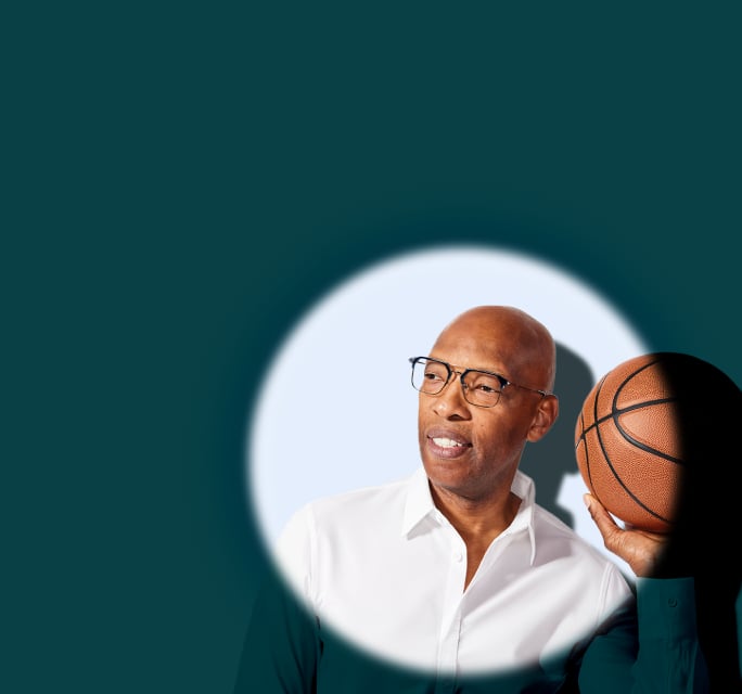 Sam Cassell holding a basketball while wearing dark rectangular sunglasses in a spotlight against a deep teal background.