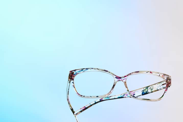 Eyeglasses with a colorful, floral pattern against a light blue and off-white gradient background.