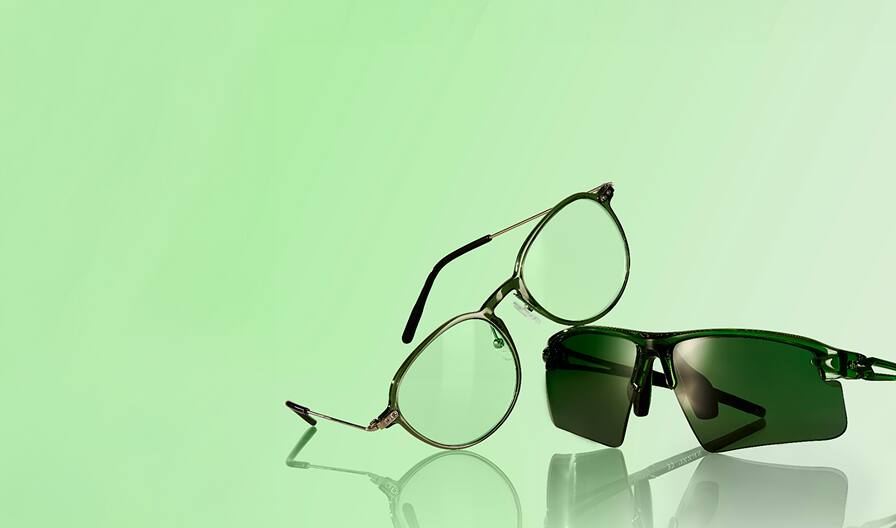 Green round glasses, style 7822624, and sport sunglasses with green-tinted lenses, style 99113124, are set against a soft green background with fresh greenery beside them.