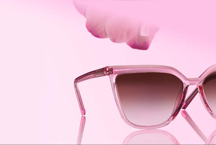 Pink cat-eye sunglasses with gradient brown lenses on a light pink background, with a pink petal in the corner.