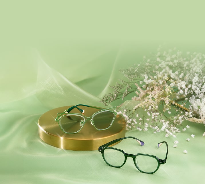 Green geometric Zenni glasses on a gold pedestal and dark green Zenni glasses on green satin.