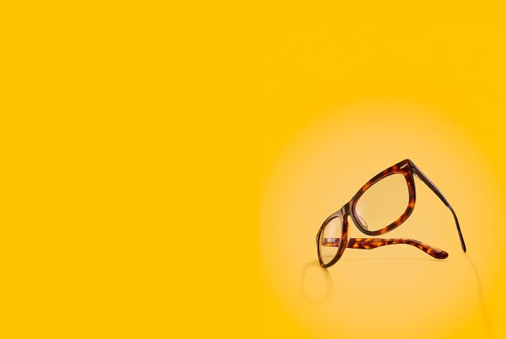 A pair of square tortoiseshell glasses floating at an angle against a solid bright yellow background.