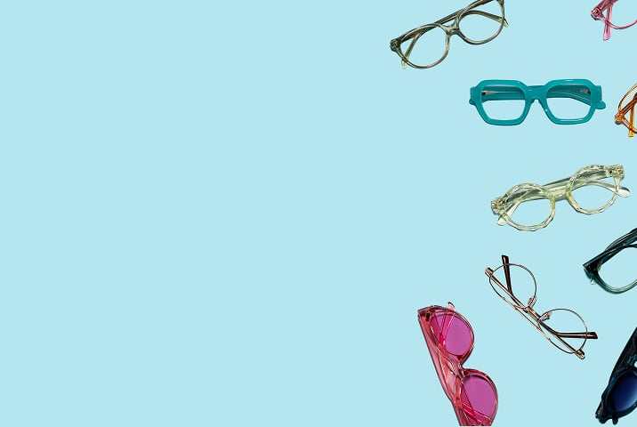 Colorful Zenni eyeglasses in various shapes and styles scattered on a light blue background, including teal, orange, purple, pink, frames, etc.