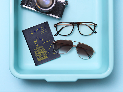 A security screening tray containing a pair of metal aviator sunglasses and a pair of tortoiseshell eyeglasses, a passport, a Zenni glasses case, and a vintage film camera.
