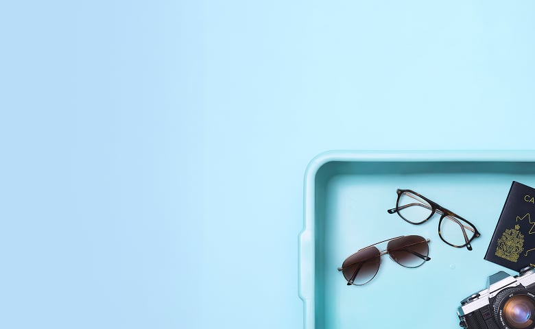 A security screening tray containing a pair of metal aviator sunglasses and a pair of tortoiseshell eyeglasses, a passport, a Zenni glasses case, and a vintage film camera.