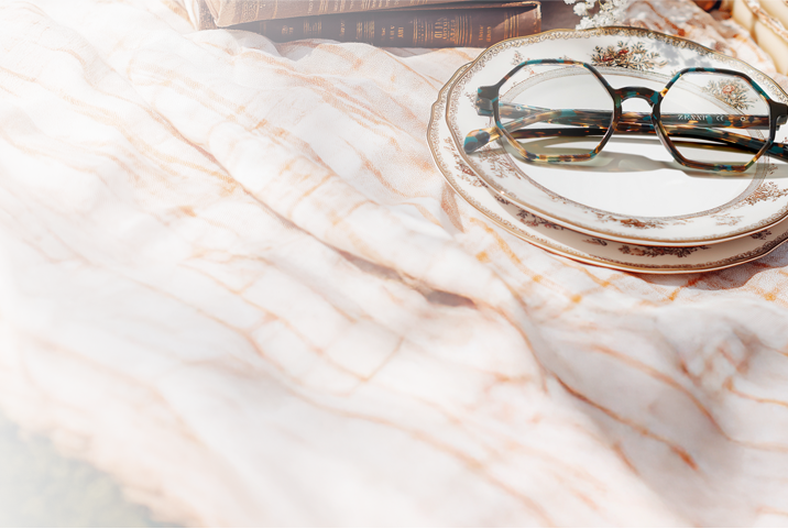 Geometric tortoiseshell frames resting on a delicate porcelain plate, nestled in a cozy picnic scene. The clear lenses and structured shape pair effortlessly with the soft textures and vintage charm of books and treats.