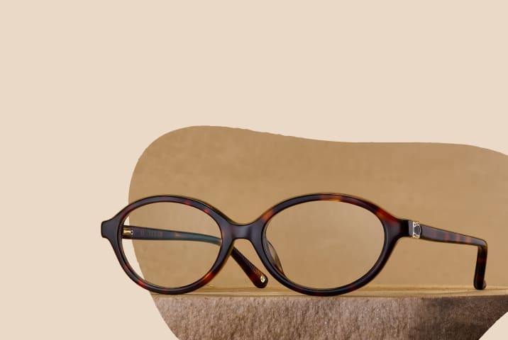 Tortoiseshell oval eyeglasses resting on a textured stone surface against a warm beige background.