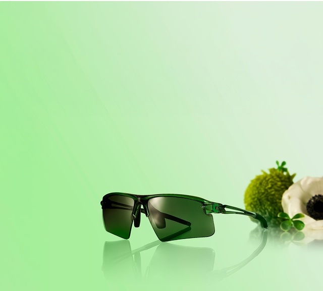 Sport sunglasses with green-tinted lenses, style 99113124, set against a soft green background with fresh greenery beside them.