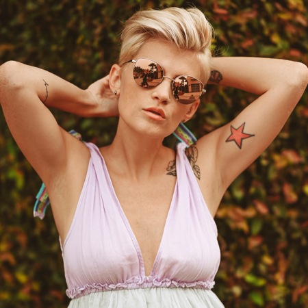 Alissa Laderer wearing zenni premium cat-eye sunglasses #1128714 in front of a tall, leafy bush.