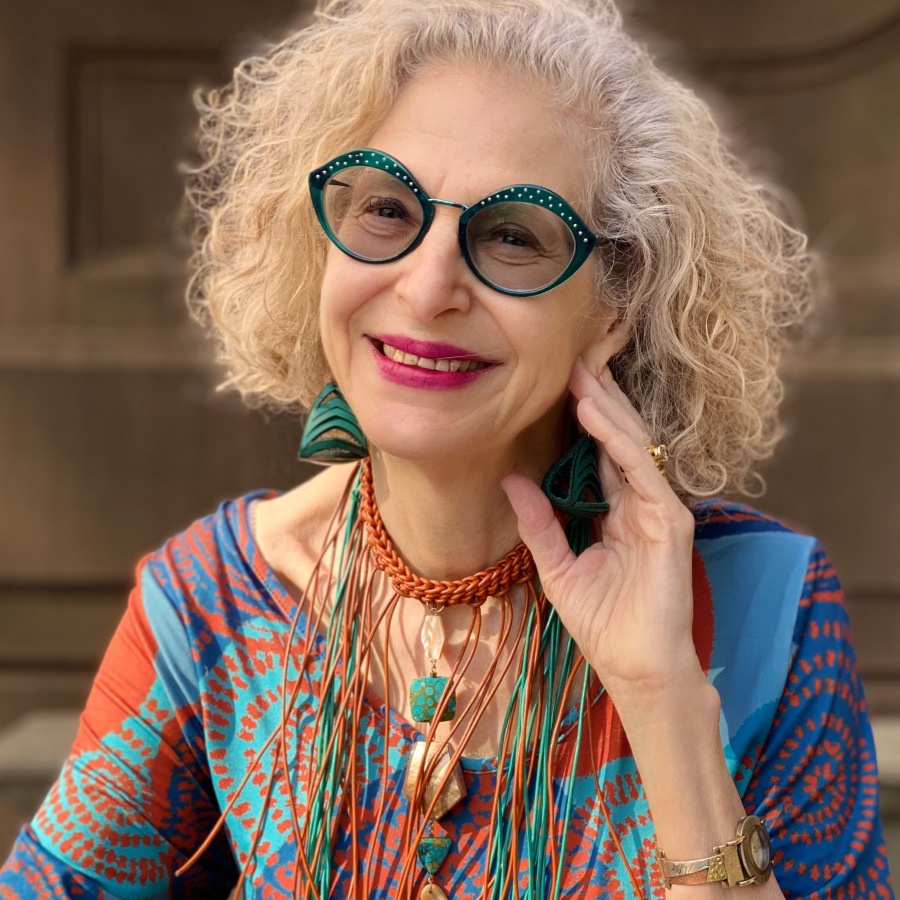 Image of a woman wearing forest green lip-shaped glasses with matching earrings and a colorful shirt.