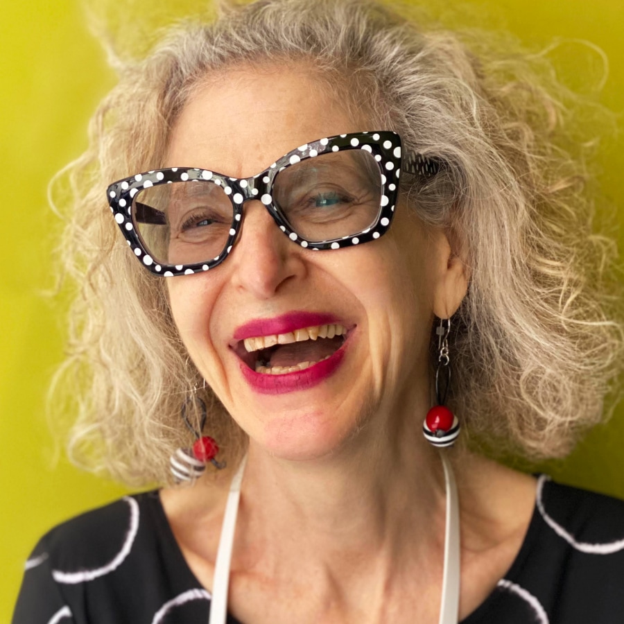 Image of a woman wearing black and white polka-dotted glasses in front of a yellow wall.