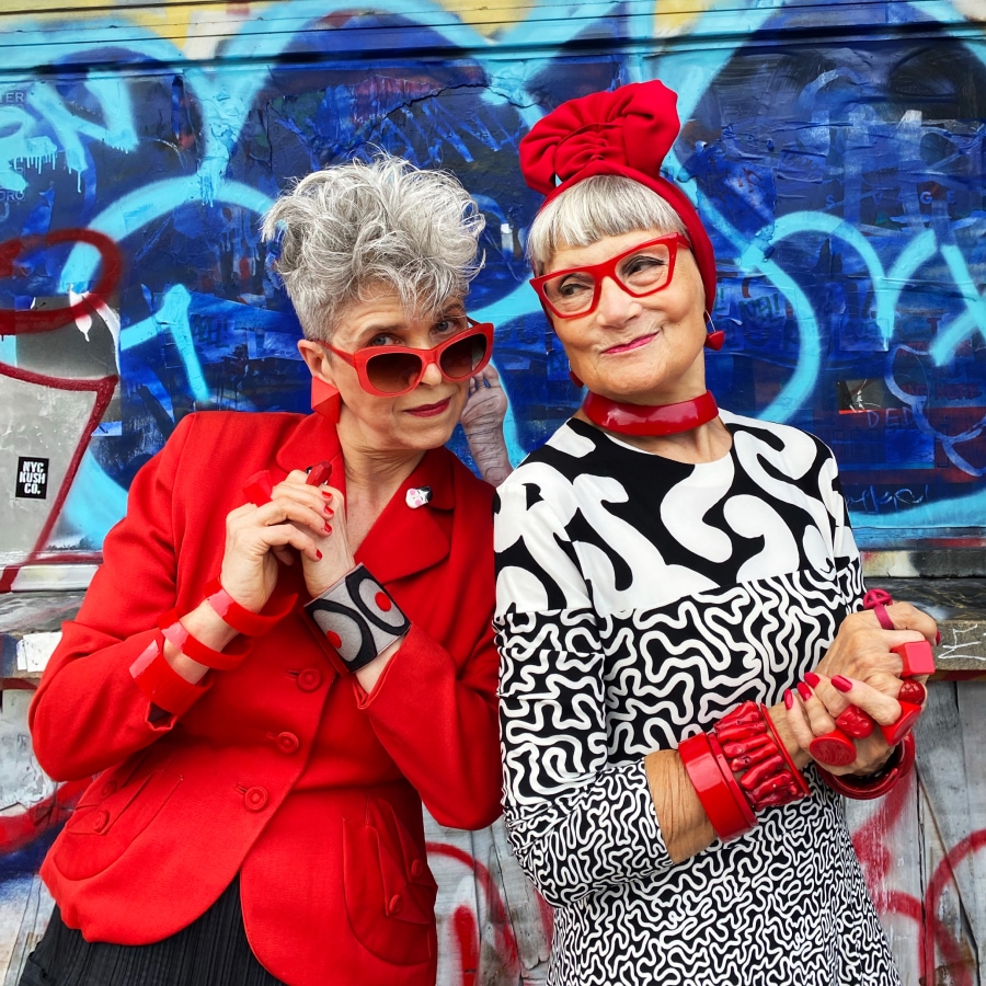 Image of two older ladies wearing bright outfits and bright red glasses.