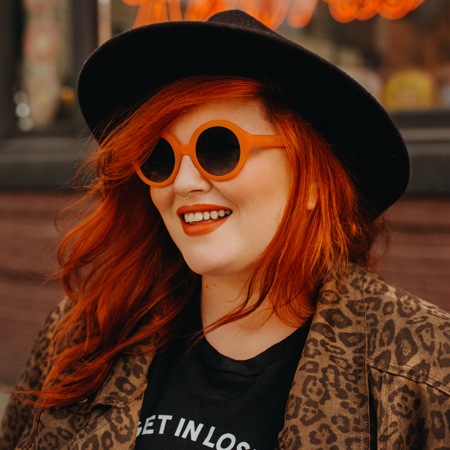 Jessy Parr wearing pico round sunglasses #4422242 in front of a blurry restaurant sign.