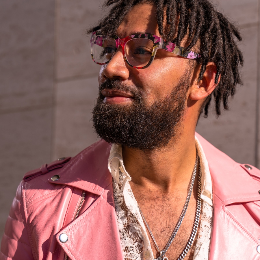 Image of a man wearing a pink leather jacket, wearing pink and purple floral glasses.